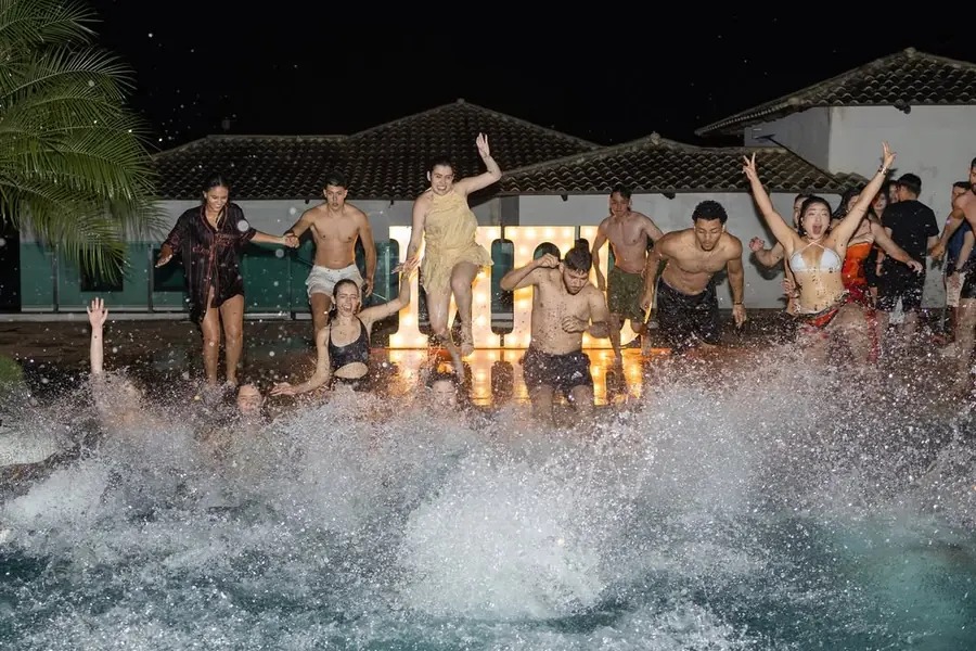 Turma pulando junta na piscina durante festa de pré-evento, à noite