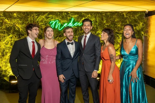 Grupo de formandos de Medicina em traje de gala diante de neon Medicina