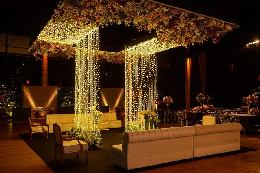 Lounge com sofás brancos sob estrutura de cortinas de luz e flores