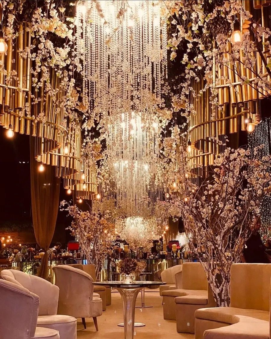 Lounge sob cascata de cristais e lustres, com poltronas e árvores floridas