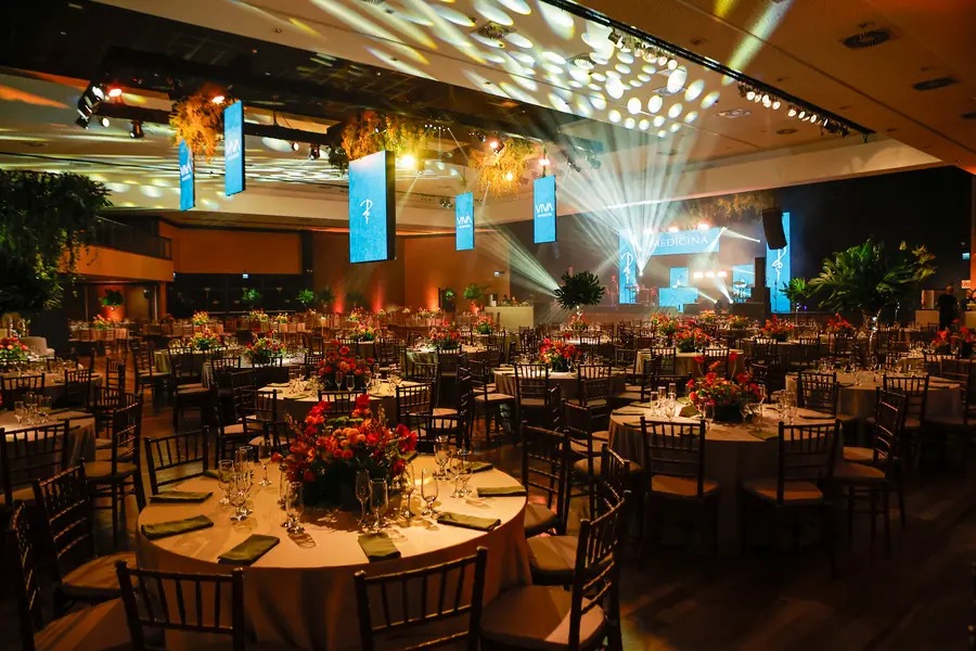 Salão de baile de Medicina montado, com mesas redondas decoradas, arranjos de flores e show de luzes no teto