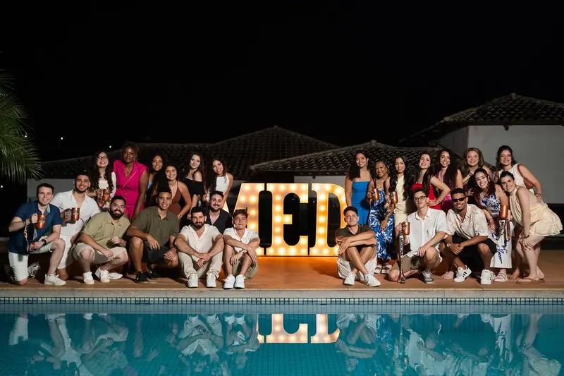 Turma de Medicina reunida à beira da piscina em pré-evento da VIVA, à noite, com letreiro MED iluminado